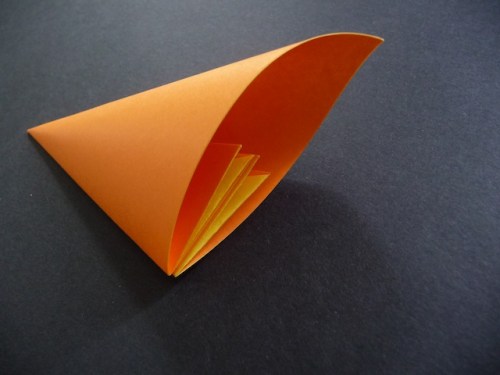 12. Apply glue or double sided tape to the outside of one of these folds. To make the petal shape, curl the paper inwards, pressing one side to the other, making sure to align the edges.